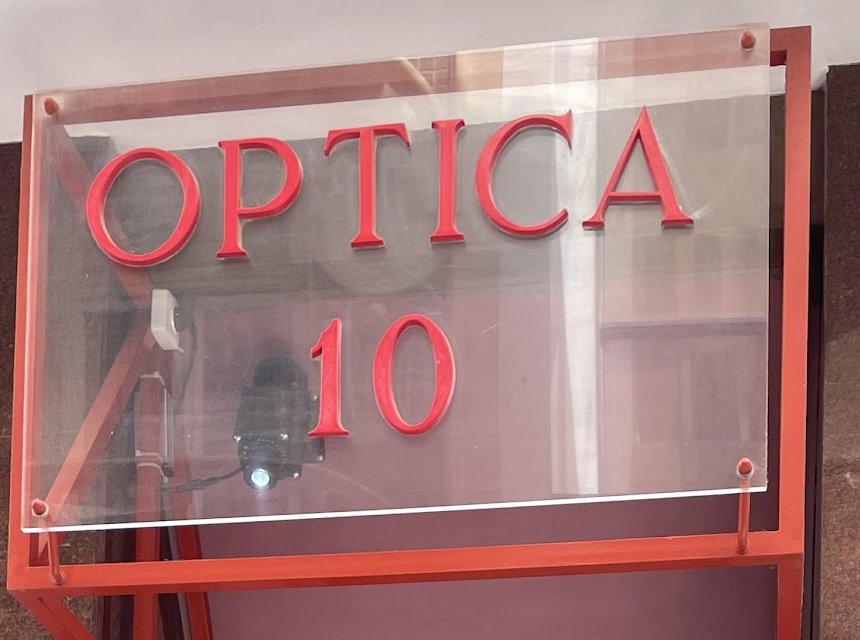 Rótulo rojo de Óptica 10 sobre la fachada de la calle Mayor